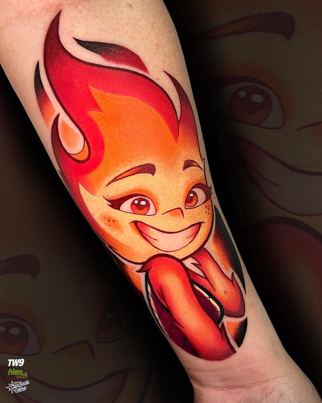 Colorful tattoo on an arm featuring a smiling character with flame-like red and orange hair, red eyes, and red clothing against skin tone.