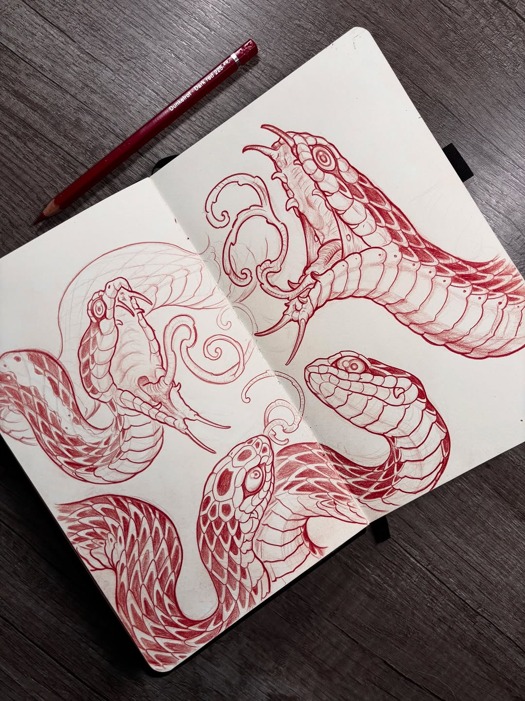 Sketch page featuring five winged serpent or dragon head designs in red pen with detailed scales, horns, and ornamental spiral patterns.