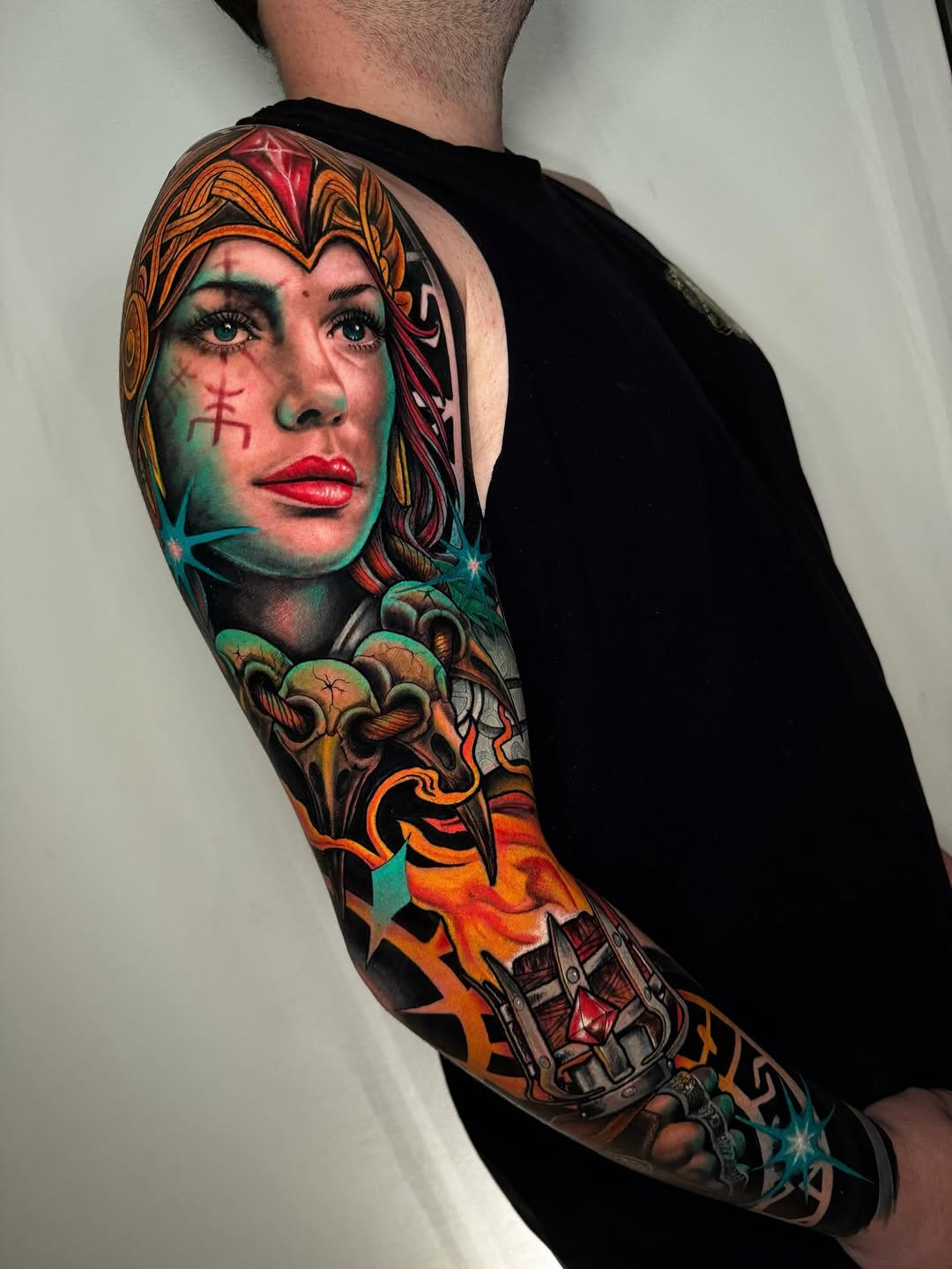 Colorful full-length arm sleeve tattoo featuring a woman's face with ornamental headdress, decorative elements, and mechanical imagery in orange, teal, red, and gold tones.