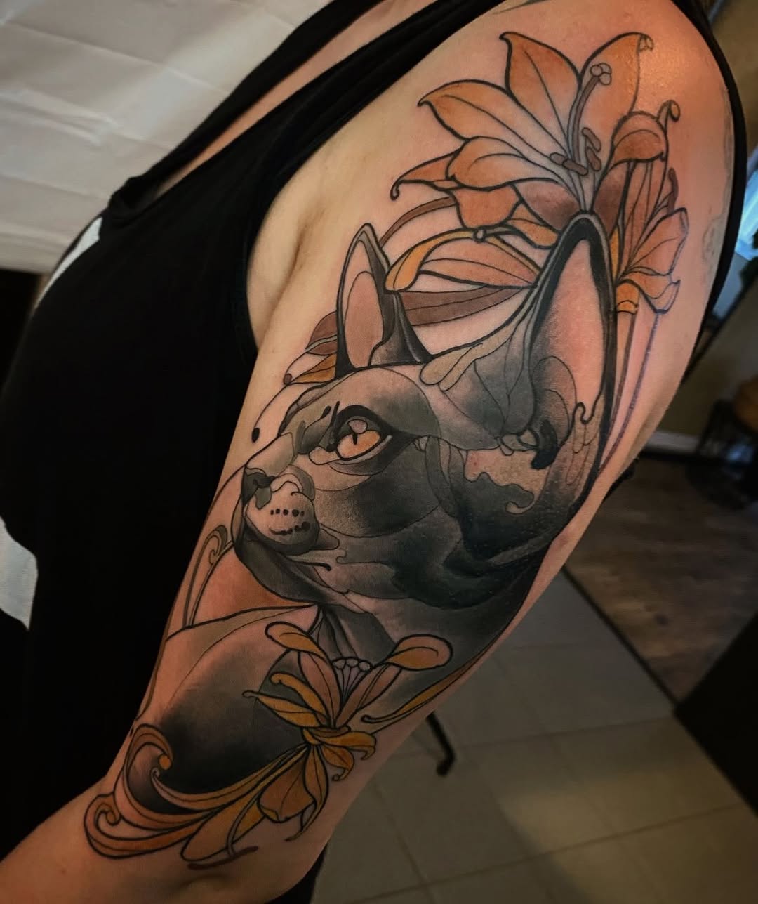 Cat's head with closed eyes surrounded by orange and yellow flowers on upper arm, with decorative scrollwork at the bottom.