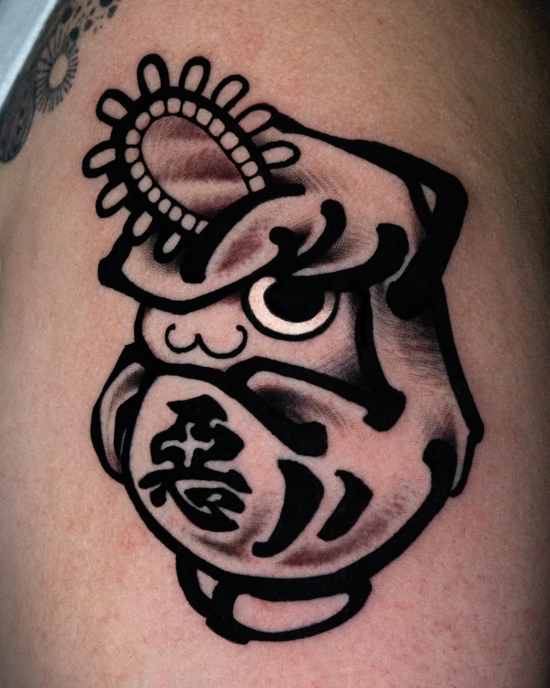 Bold black-outlined abstract face with decorative circular crown and organic shapes, displayed on pale skin with subtle shading and dimension.