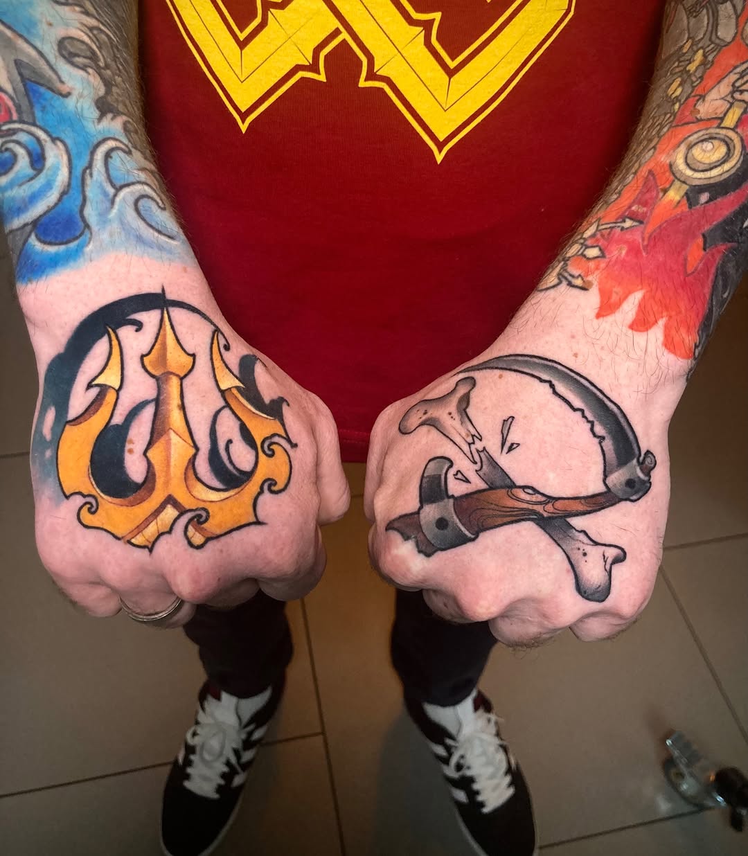 Two hands displaying matching tattoos: an orange flame design on the left hand and a grey whale on the right hand, with colorful sleeve work visible on the arms.
