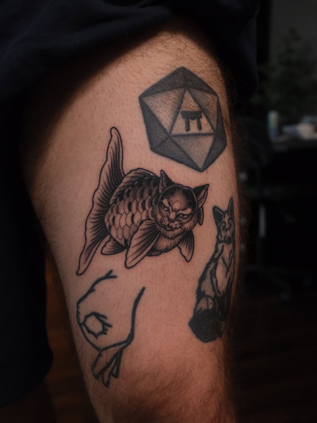 Tattoo on upper arm featuring a winged cat with detailed linework, a geometric polyhedron shape, and additional animal figures in black ink.